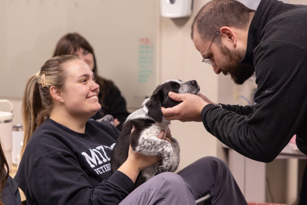 Don Cherry petting a puppy held by a student.