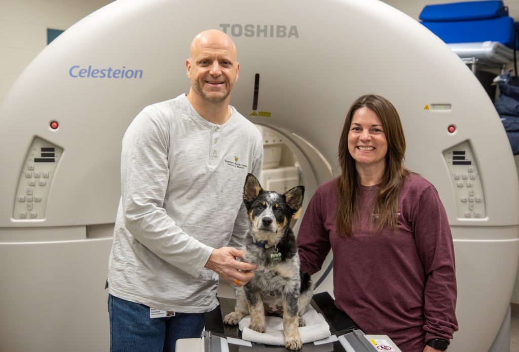 Kevin and Joni Lunceford pictured with a dog in front of the PET-CT scanner.