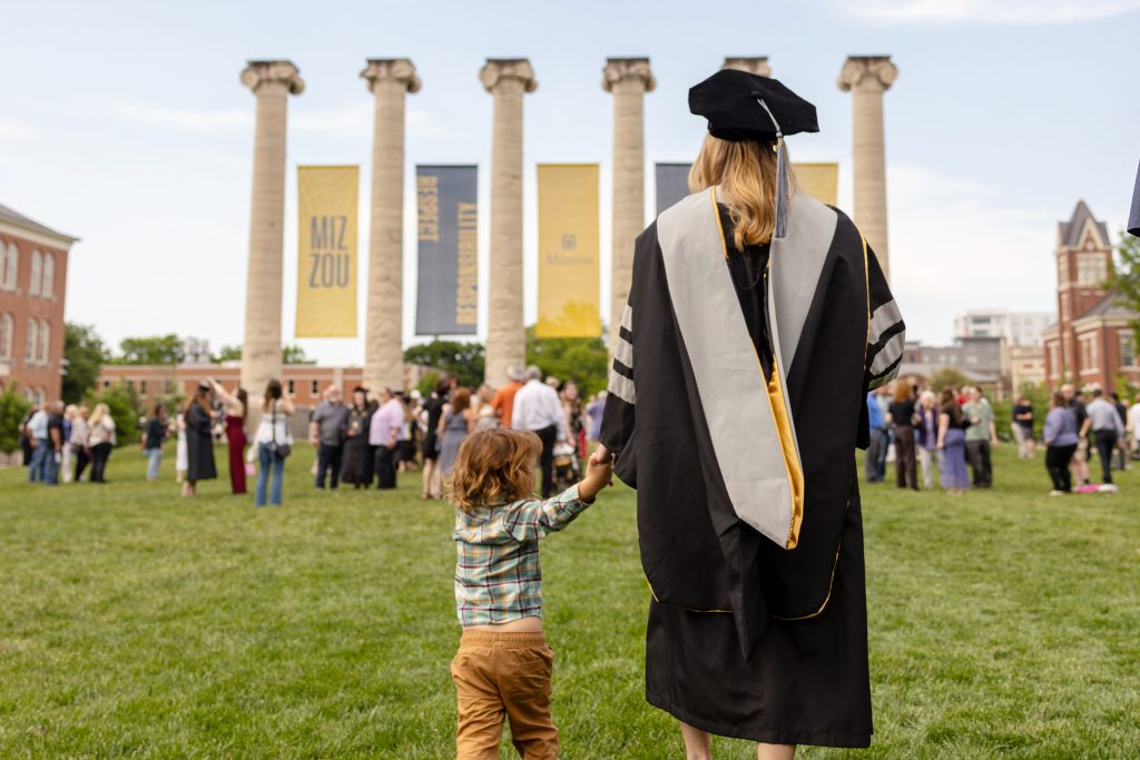 a student walks with a toddler in front of the columns