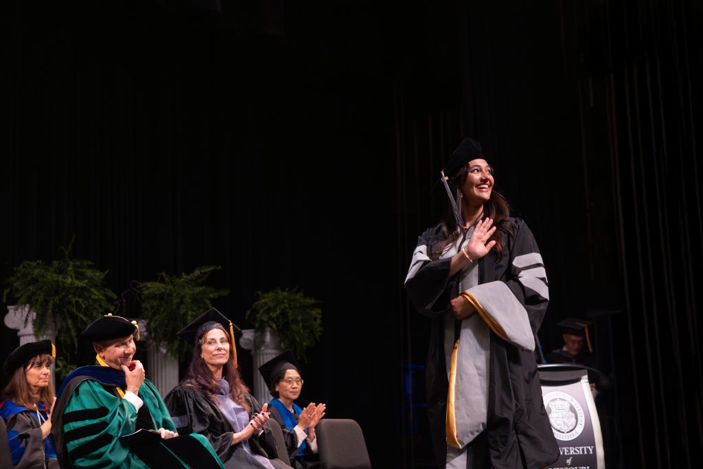 a student smiles and waves while crossing the stage