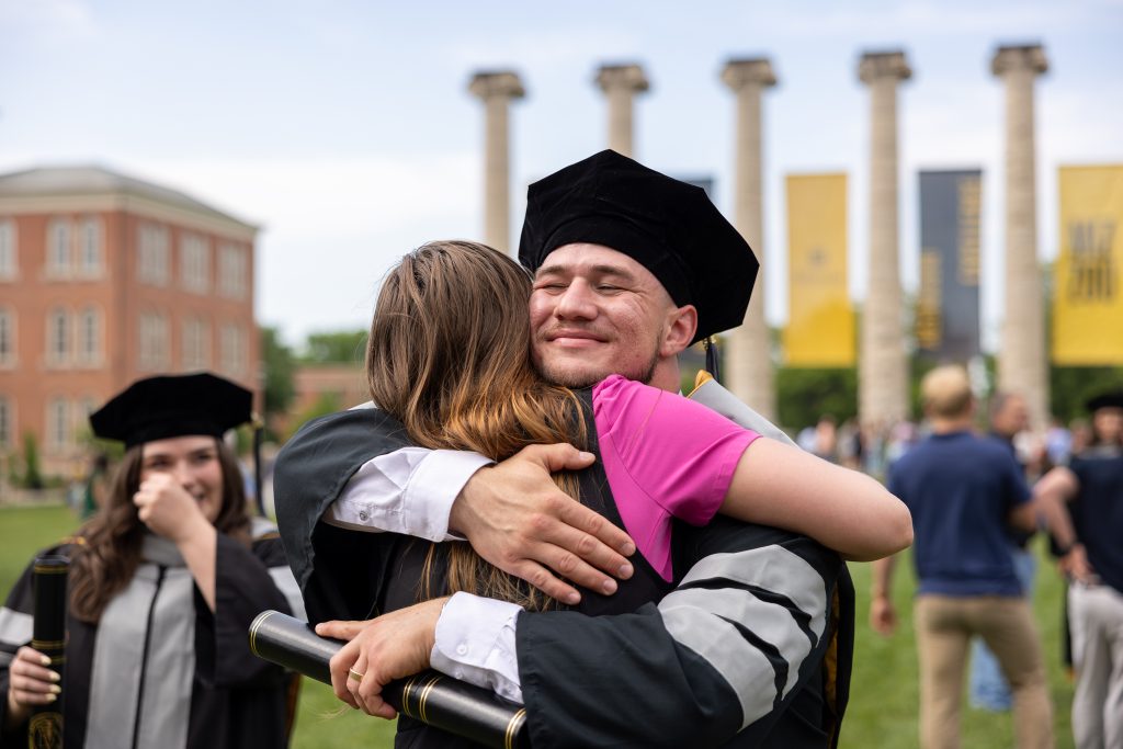 a student hugs a family member after commencement in front of the columns