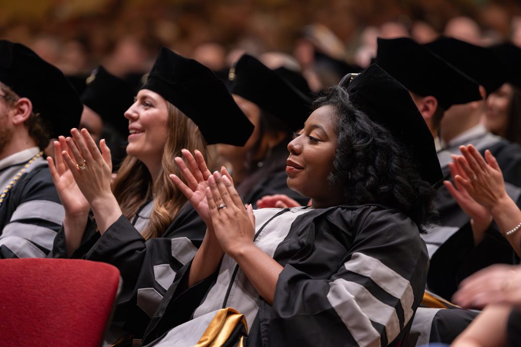 students smile and clap from the audience during commencement