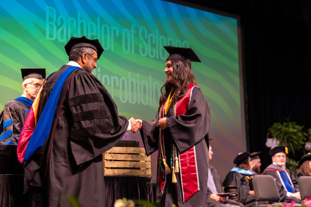 a student smiles and receives her diploma from the dean