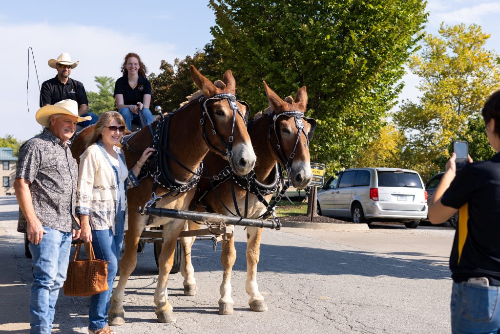 two people take a photo with the mules/wagon